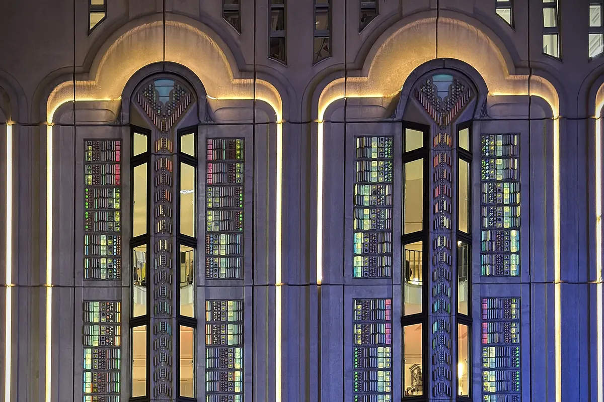 Two arched windows with stained glass lit in blue and gold on the stone facade of a theatre at night