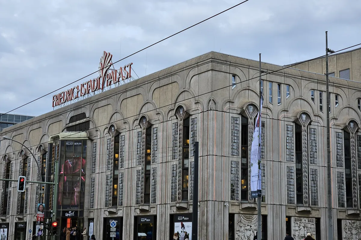The stone front of a large theatre building on a Berlin street corner, with tram wires above the road and a sign on the roof